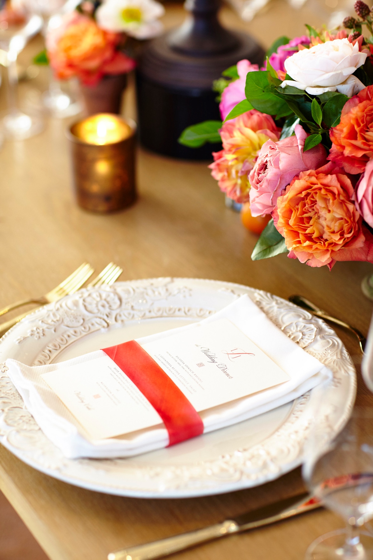 Elegant tablescape with vibrant pink and coral florals, glowing candles and polished table settings