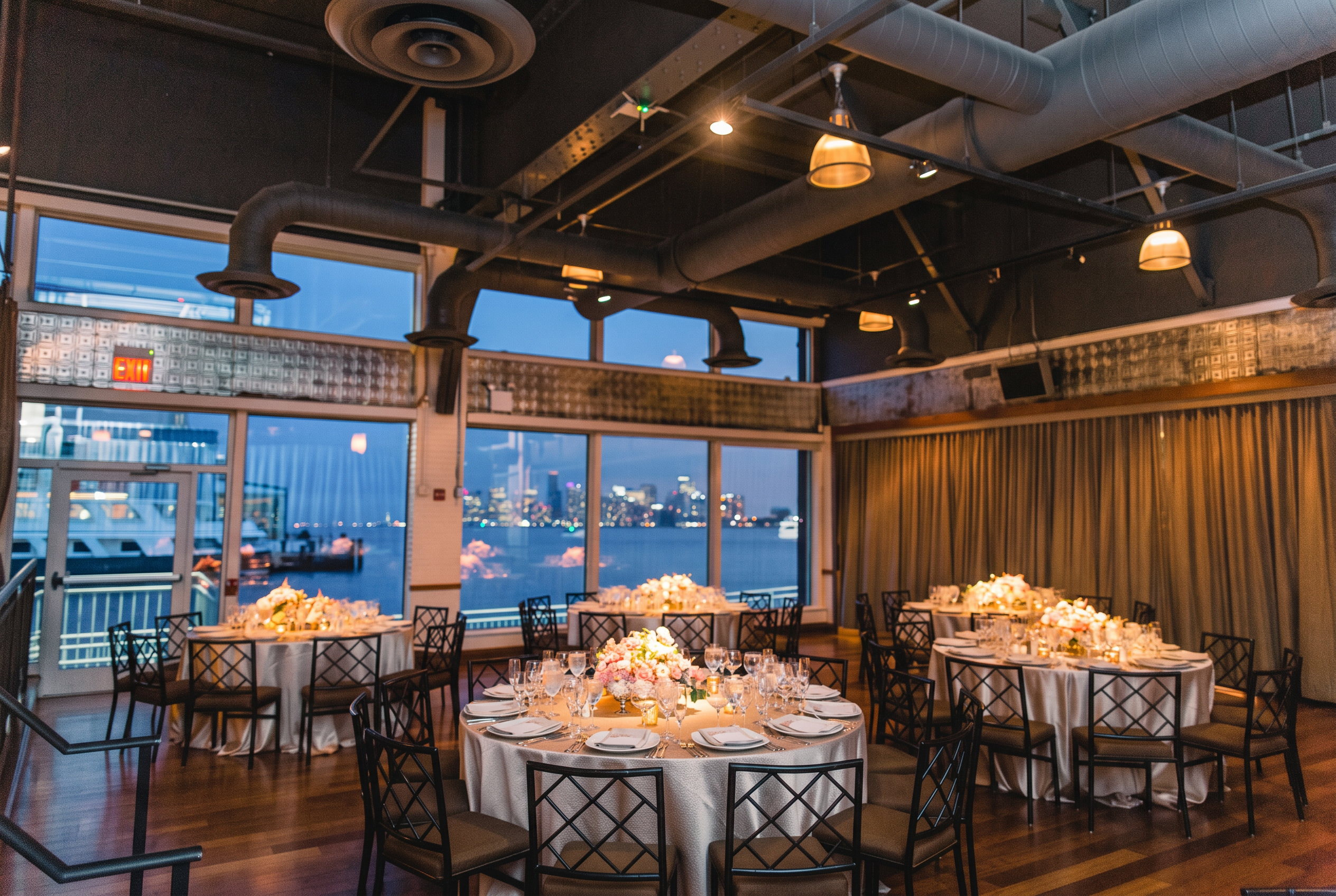 Elegant waterfront reception room with round tables, floral centerpieces, and city skyline views